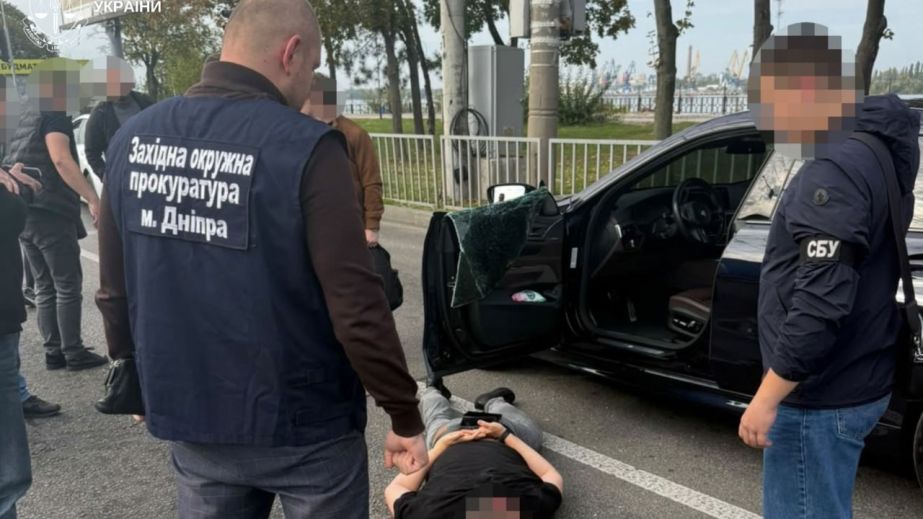 Правоохоронці біля службового автомобіля під час обшуку в міському кварталі